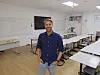 Mann steht in hellem seminarraum mit Tischen, Stühlen, Whiteboard und Bildschirm.