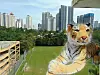 Große Tiger-Skulptur vor grünem Sportfeld und Hochhäusern im Hintergrund.