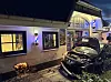 Schwarzer Wagen nach Unfall vor beleuchtetem Eingang, Trümmer und beschädigte Front auf dem Gehweg.