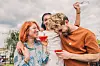 Drei junge Menschen stoßen im Freien mit Cocktails an und umarmen sich.