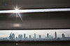 Helle Jalousien schirmen ein Bürofenster ab, dahinter eine Stadt-Skyline in der Ferne.