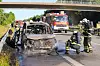 Feuerwehrleute sichern ein ausgebranntes Auto auf der Autobahn, im Hintergrund ein rotes Löschfahrzeug.