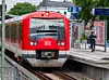 Roter DB-Regionalzug hält am Bahnsteig, ein Fahrgast wartet daneben.