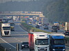 Dichter Verkehr mit Lastwagen und Pkw auf einer Autobahn unter einer Brücke.