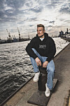 Hauke Wahl sitzt an den Hamburger Landungsbrücken mit Blick auf Hafen, Wasser und Kräne.