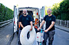 Zwei Techniker vor einem offenen Transporter mit Kabeltrommel und Werkzeugkisten auf einer Straße.