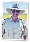 Ranger in heller Uniform mit Hut und Sonnenbrille vor grüner Landschaft und blauem Himmel.