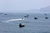 Mehrere Handelsschiffe und Boote vor Khasab, ein Schnellboot zieht eine weiße Spur durchs Meer.