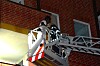 Feuerwehrkräfte stehen auf einer Drehleiter an einer Backsteinfassade bei Nacht.