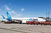 AJet-Flugzeug auf dem Vorfeld mit roten Bodenfahrzeugen und Serviceausrüstung unter blauem Himmel.