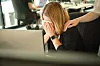 Frau am Schreibtisch mit bedecktem Gesicht, eine Hand liegt tröstend auf ihrer Schulter im Büro.