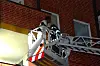 Drehleiter der Feuerwehr vor roter Backsteinfassade hebt Einsatzkraft zum Fenster.