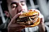 Mann hält nah an der Kamera einen Burger mit Sesambrötchen und Patty.