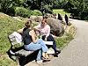 Zwei Frauen sitzen auf einer Parkbank am Weg und sprechen im Grünen.