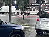 Person steht auf Verkehrsinsel an nasser Kreuzung zwischen Autos und Lieferwagen.