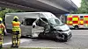 Schwer beschädigter weißer Transporter unter einer Autobahnbrücke, Rettungskräfte und Einsatzfahrzeug daneben
