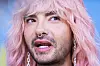 Bill Kaulitz mit rosa Haaren, Nasenpiercing und offenem Mund vor blauem Hintergrund.