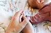 Mutter und Vater berühren die Hand ihres wenige Wochen alten Babys auf einer Decke.