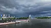 Gewitterwolken über Wasser, am Ufer Flaggen und ein Springbrunnen in der Ferne.