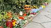 Blumen, Kerzen und Andenken sind entlang eines Gehwegs vor einer Hecke niedergelegt.