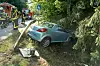 Auto liegt im Graben neben der Straße, Einsatzkräfte und Feuerwehrfahrzeuge im Hintergrund.