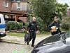 Polizisten sichern einen abgesperrten Bereich vor einem Wohnhaus und tragen Ausrüstung.