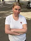 Frau in weißem T-Shirt mit rotem Herz-Symbol steht draußen mit verschränkten Armen.
