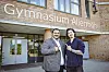 Julian Lee und ein Haspa-Mitarbeiter stehen vor dem Gymnasium Allermöhe und zeigen aufeinander.