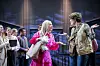 Frau in Pink und Mann in Goldgestik auf einer Bühne vor Zuschauern.