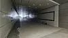 Leerer heller Tunnelgang mit großer schwarzer Anzeige an der rechten Wand und Licht am Ende des Korridors.