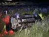 Auto liegt nachts im Gras auf der Seite, rote Einsatzlichter beleuchten die Unfallstelle.