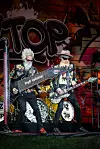 Zwei Musiker mit Gitarren vor einem Graffiti-Backdrop mit großem „Top“-Schriftzug auf der Bühne.