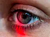 Nahaufnahme eines Auges mit rotem Licht und Spiegelung im Blick.