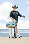 Erling Haaland am Flughafen in Dallas mit Koffer und Reisetasche vor blauem Himmel.