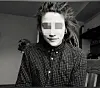 Person mit kariertem Hemd sitzt in einem Innenraum und schaut in die Kamera.