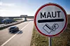 Mautschild an der Autobahn, im Hintergrund vorbeifahrende Autos und eine Brücke.