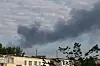 Schwarze Rauchwolke über Belgorod nach einem Raketenangriff, Häuser und Bäume im Vordergrund.