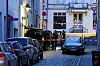 Polizeibeamte stehen hinter Absperrband in einer engen Straße mit geparkten Autos und Wohnhäusern.