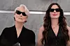 Miranda Priestly und Andie Sachs stehen nebeneinander vor grauem Hintergrund.