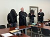 Vier Männer stehen in einem Besprechungsraum am Tisch, einer mit Jacke über dem Kopf.