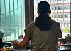 Person sitzt am Tisch vor großem Fenster mit Blick auf Bürogebäude; Essen und Utensilien liegen daneben.