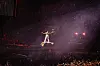 Person in heller Kleidung auf dunkler Bühne unter dichtem Konfettiregen und rotem Licht in einer Arena.