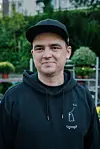 Mann mit schwarzer Kappe und Hoodie vor grünem Hintergrund
