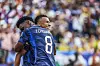 Mbappé und Tchouaméni feiern gemeinsam im Trikot von Frankreich vor unscharfem Stadionpublikum.