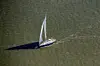 Segelboot mit weißen Segeln auf ruhigem Wasser, langer Schatten links.