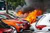 Zwischen parkenden Autos brennt ein Wagen, Flammen und dichter schwarzer Rauch steigen auf.