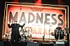 Madness auf einer Konzertbühne mit Schlagzeug, Percussion und großem LED-Schriftzug im Hintergrund.