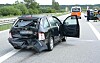Beschädigter Pkw auf der Autobahn, Tür offen, Einsatzkräfte sichern die Unfallstelle im Hintergrund.