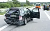 Beschädigter Pkw auf der Autobahn, Tür offen, Einsatzkräfte sichern die Unfallstelle im Hintergrund.