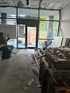 Leerer Ladenraum mit Paletten, Baustellenresten und geöffneten Glastüren zum Außenbereich.